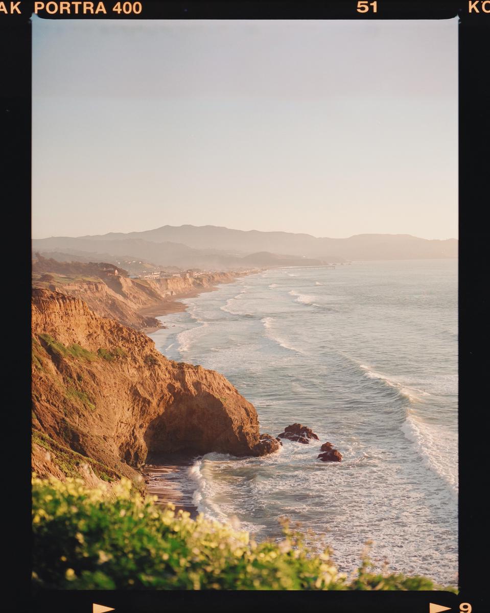 A long stretch of coastline with cliffs and waves is visible under a hazy sky.