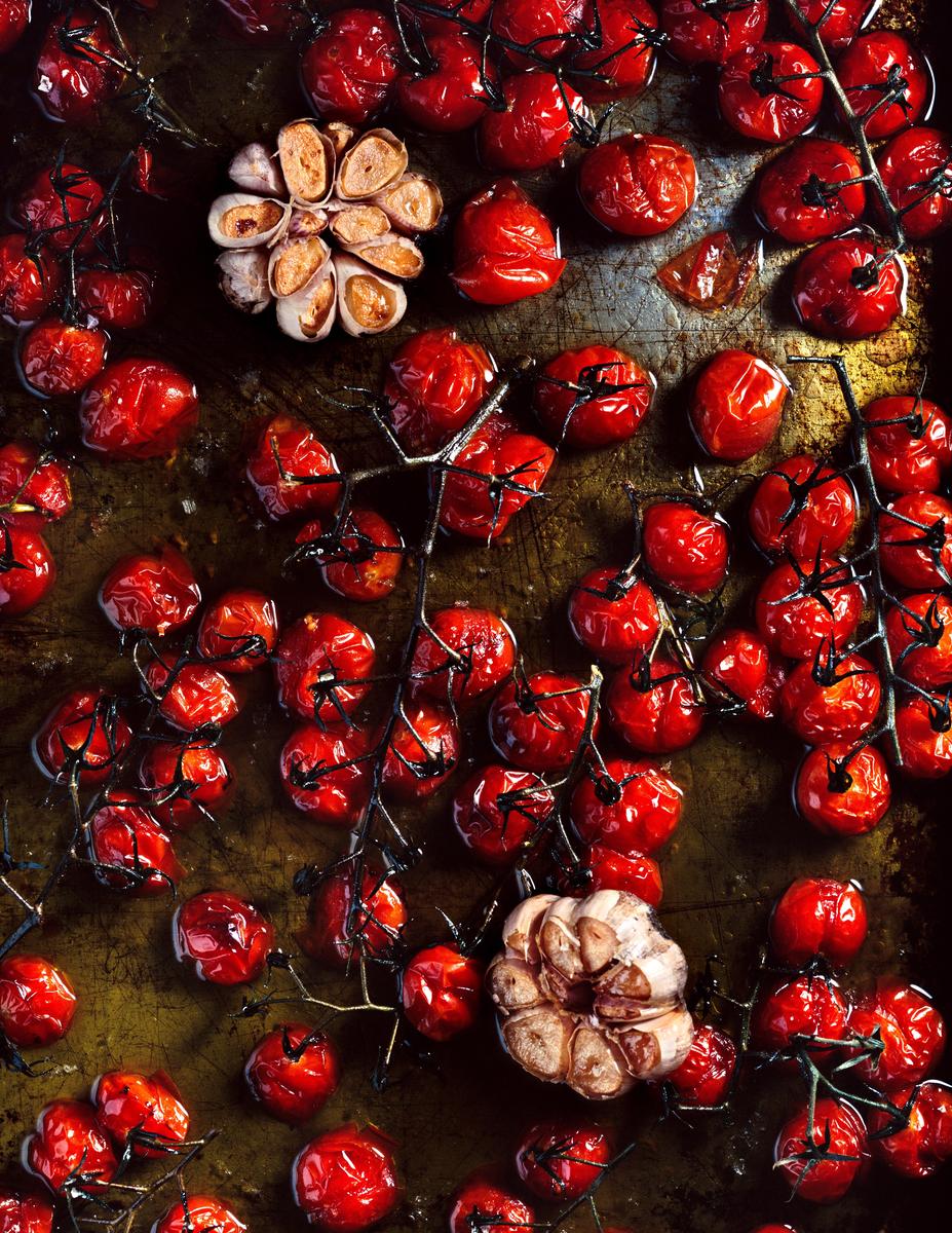 Roasted cherry tomatoes on the vine and two heads of garlic are arranged on a baking sheet.