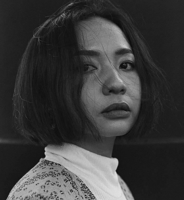 A woman with short hair and a turtleneck sweater looks directly at the viewer.