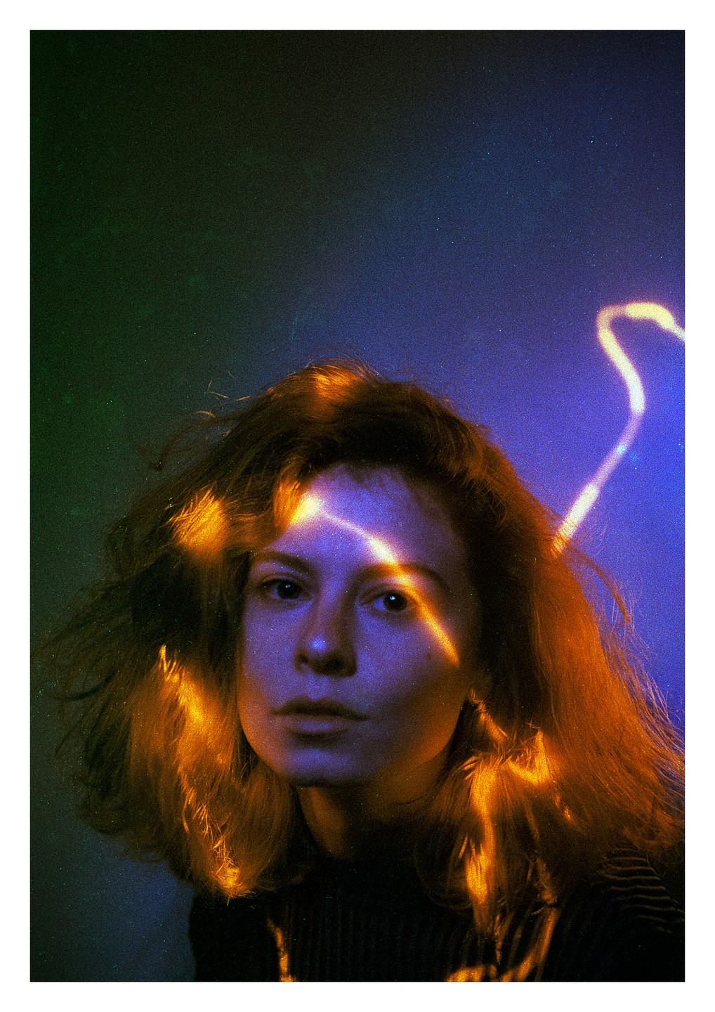 A woman with long hair looks directly at the viewer, with a beam of light across her face and hair.
