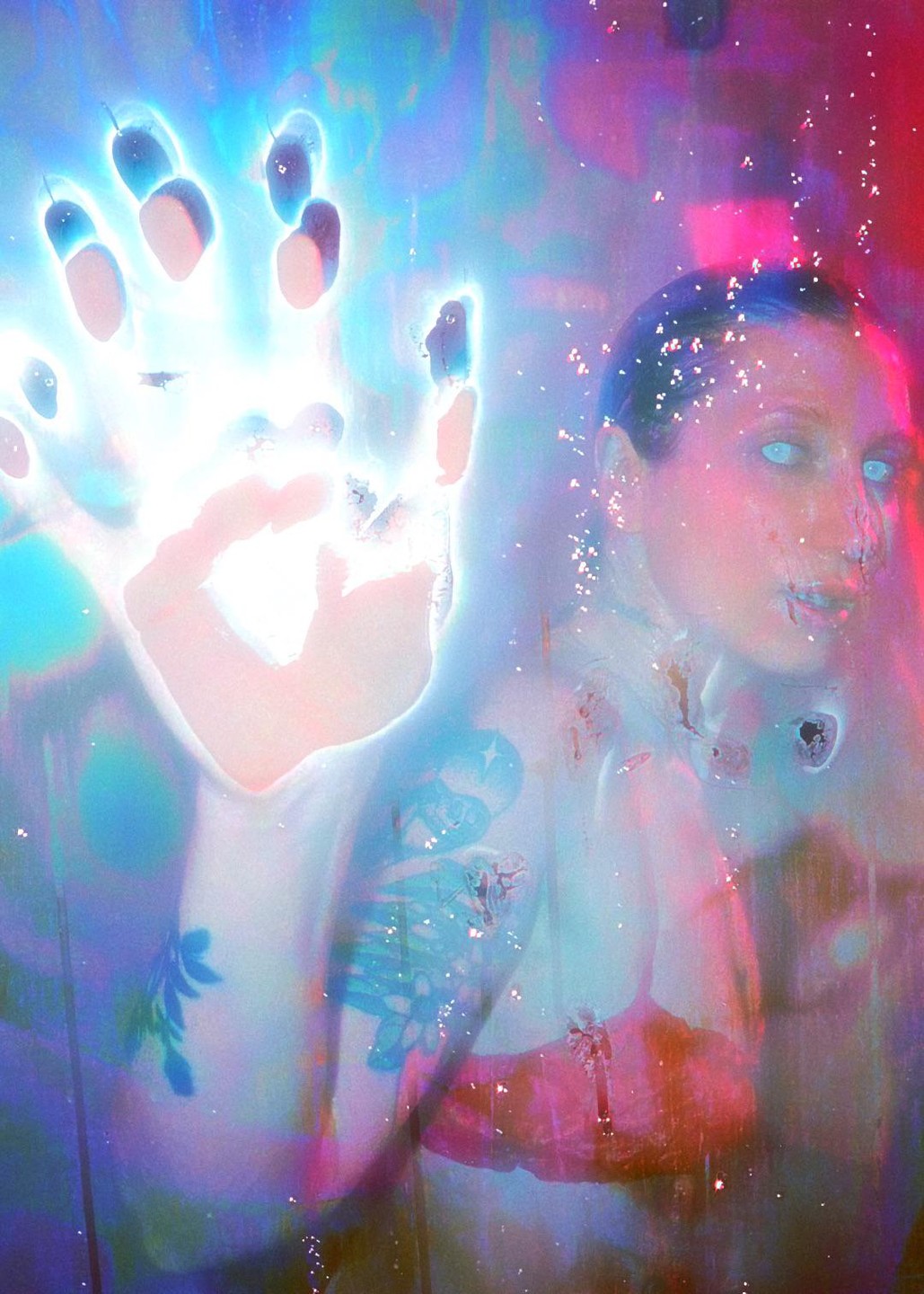 A woman with glowing blue eyes and tattoos on her arm is visible through a bright, glowing handprint.