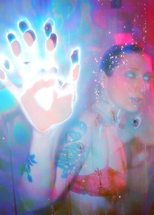 A woman with glowing blue eyes and tattoos on her arm is visible through a bright, glowing handprint.