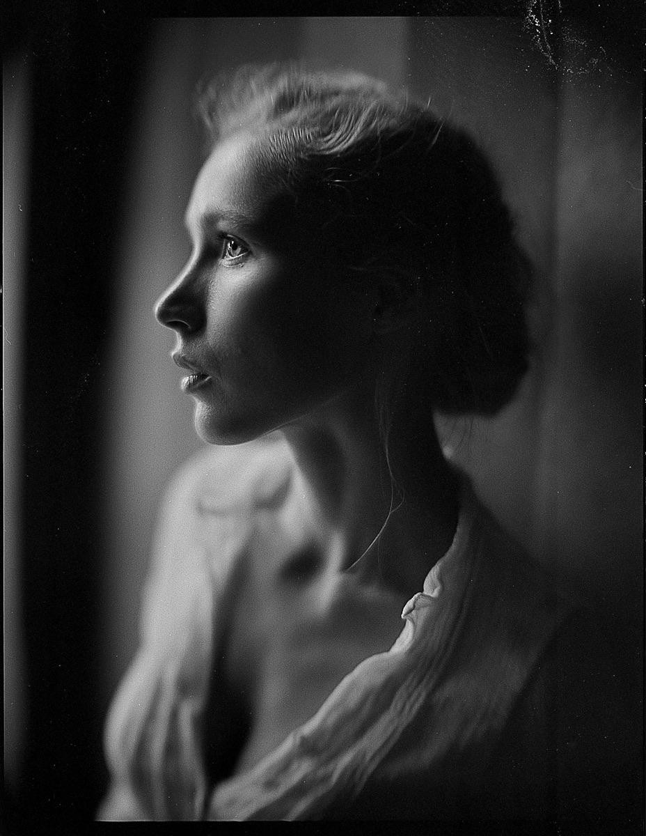 A woman is captured in a black and white profile portrait, looking upwards with soft light illuminating her face.