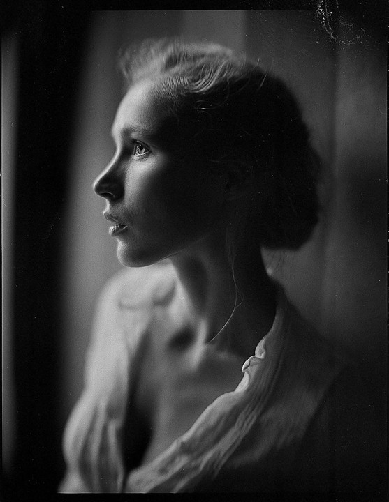 A woman is captured in a black and white profile portrait, looking upwards with soft light illuminating her face.