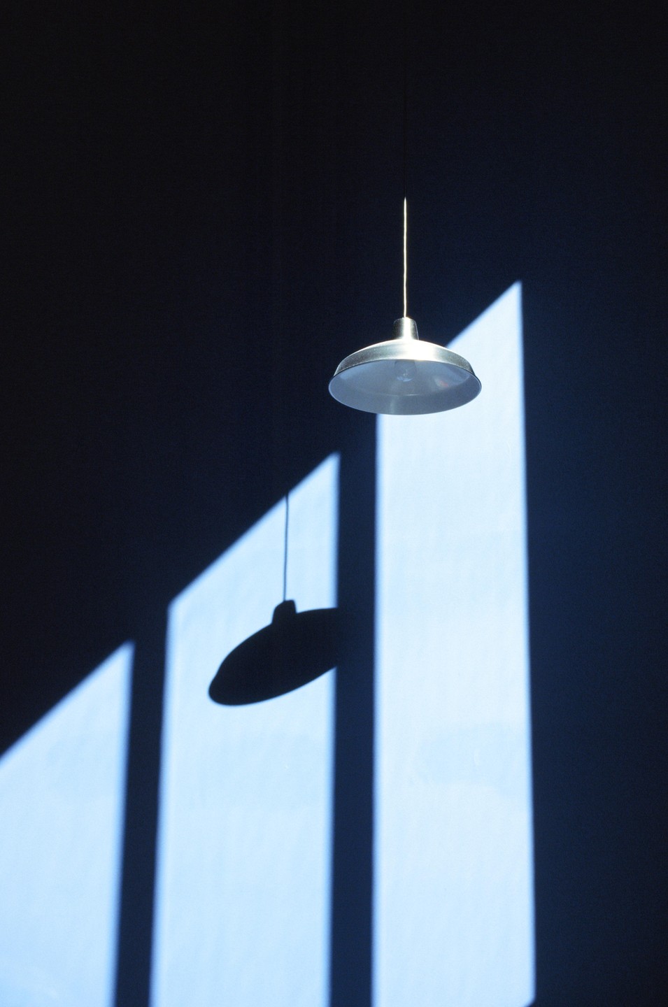 A hanging lamp casts a shadow on a wall with geometric light patterns.