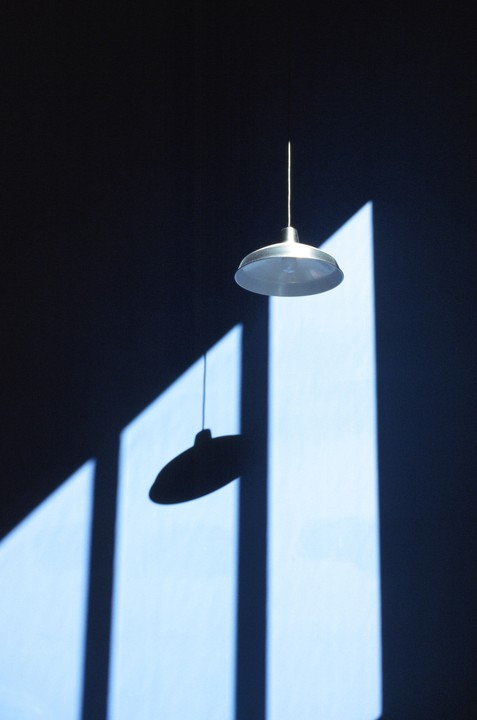A hanging lamp casts a shadow on a wall with geometric light patterns.