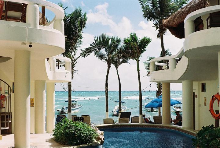 A resort with a swimming pool and palm trees overlooks the ocean with boats.
