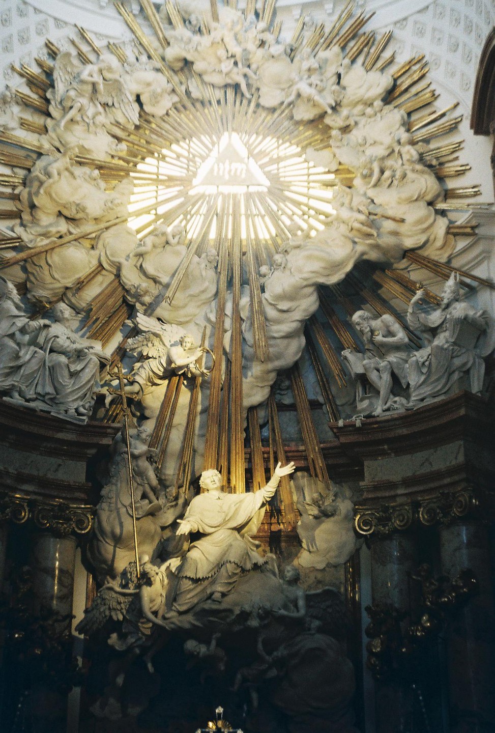 A large, ornate sculpture of figures and clouds with golden rays emanating from a central triangle is visible inside a building.