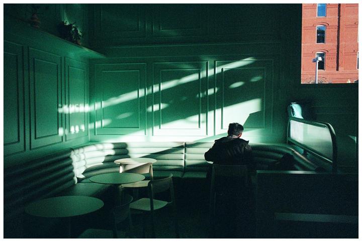 A man sits at a table in a green-paneled room with sunlight streaming through a window.