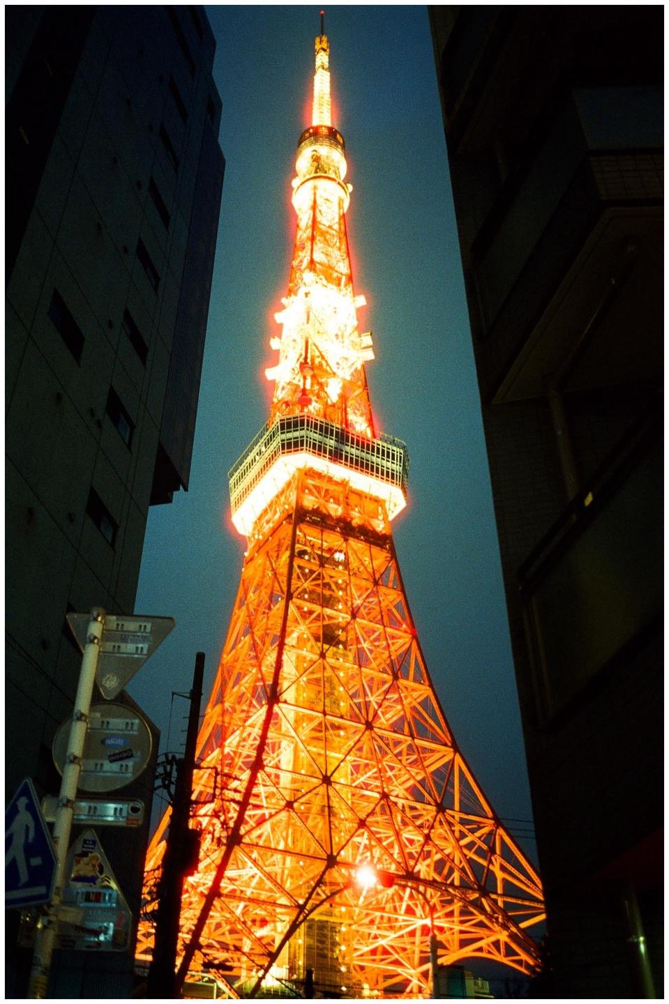 The Tokyo Tower is illuminated in orange and stands tall between two dark buildings at night.