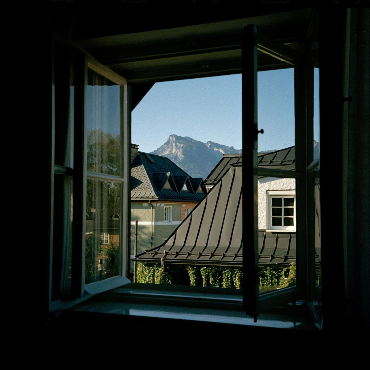 A view through an open window shows rooftops and a mountain under a clear sky.