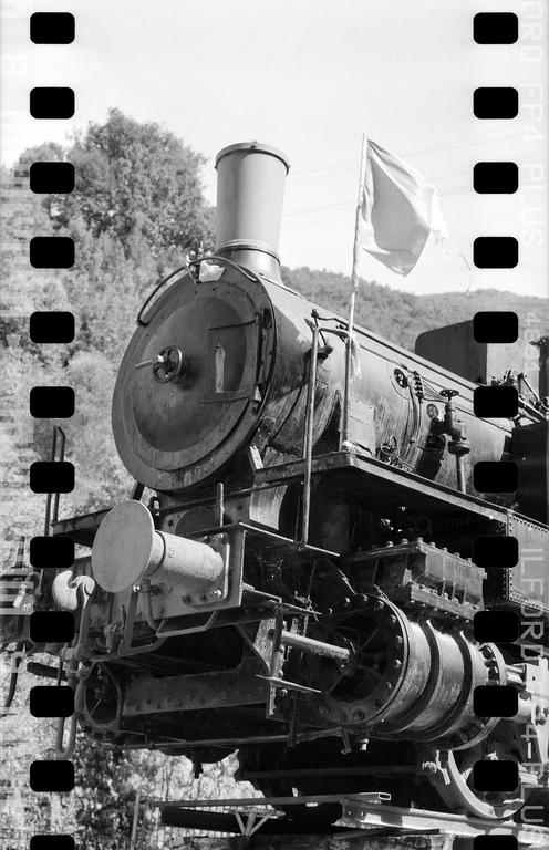 A large, old steam locomotive with a flag on its front is parked outdoors.