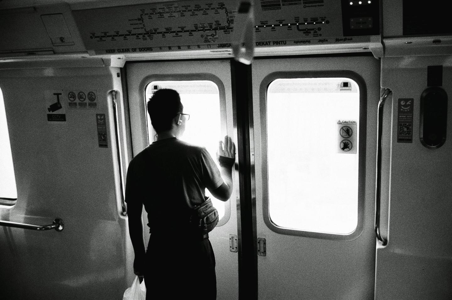 A man stands with his back to the camera, looking out a brightly lit train door.