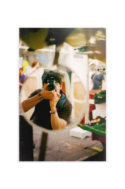 A man is taking a self-portrait in a mirror at a market.