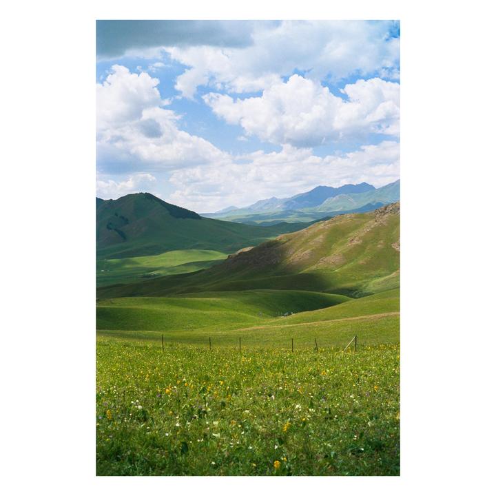 A vast green valley with rolling hills and mountains under a cloudy sky.