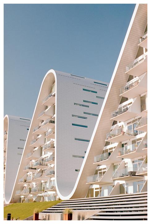 Three modern white buildings with curved roofs and balconies are visible under a clear blue sky.