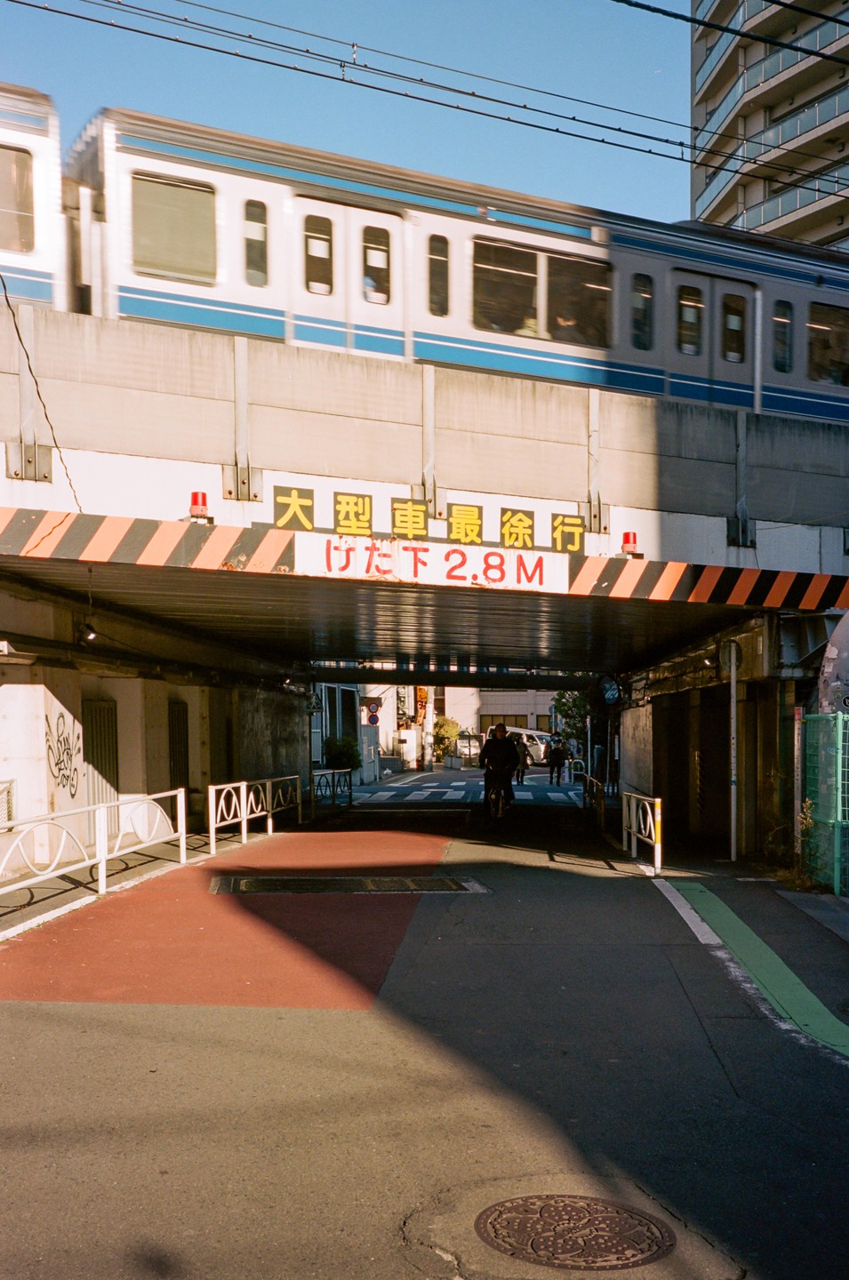 A train passes over a street with a man on a bicycle riding through a tunnel.
