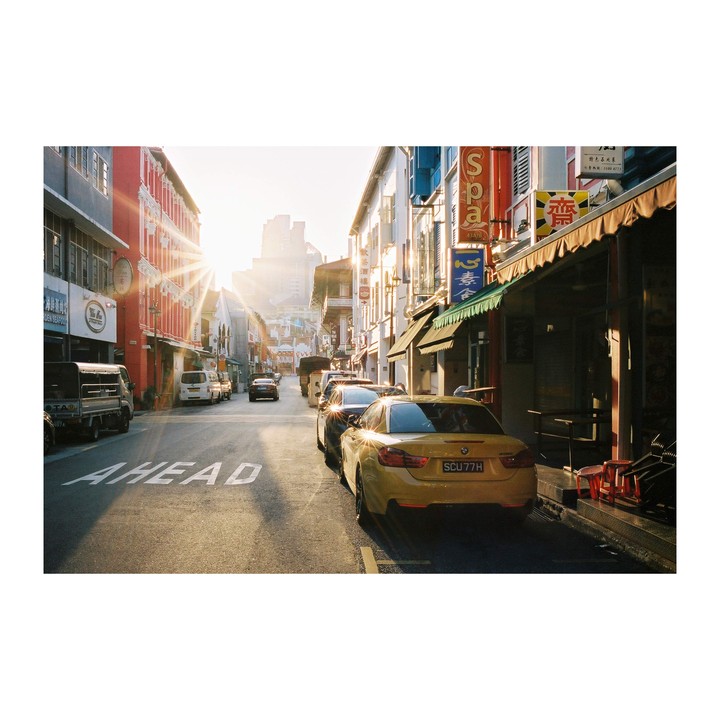 A street with parked cars and buildings on both sides is illuminated by the morning sun.