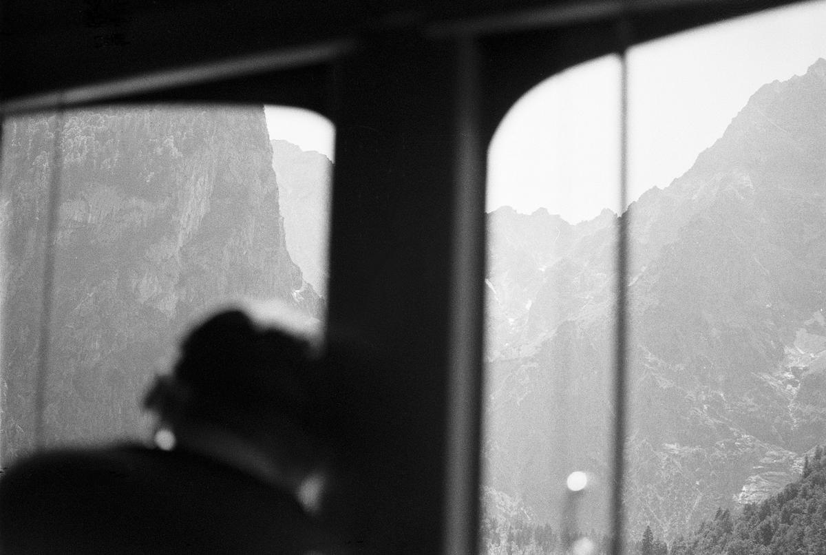A blurry person sits in a vehicle looking out a window at a mountain range.