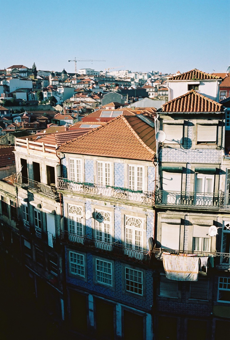 A high-angle view shows the tiled facades and terracotta roofs of buildings in Porto under a clear sky.