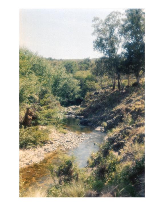 A narrow stream flows through a lush, green landscape under a bright sky.