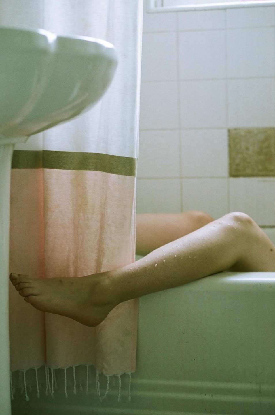 A person's wet leg and foot extend from a bathtub, with a shower curtain and sink visible in the foreground.