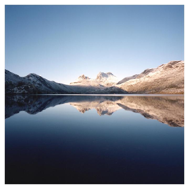 Snow-covered mountains are reflected in the still water of a lake under a clear sky.