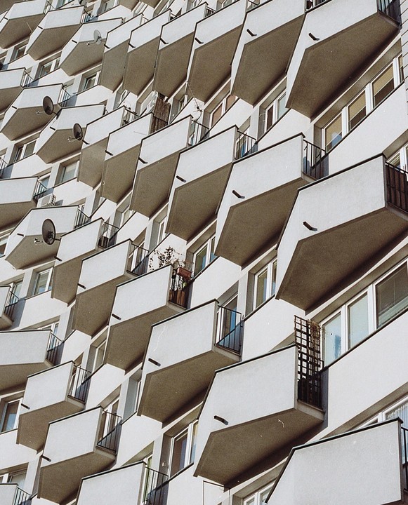 A building with many balconies and satellite dishes is shown from a low angle.