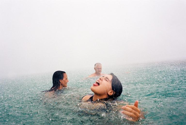 Three people are swimming in the ocean during a rainstorm.