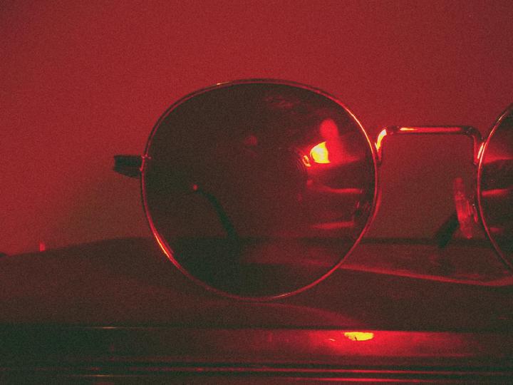 A pair of round glasses is illuminated by a red light.