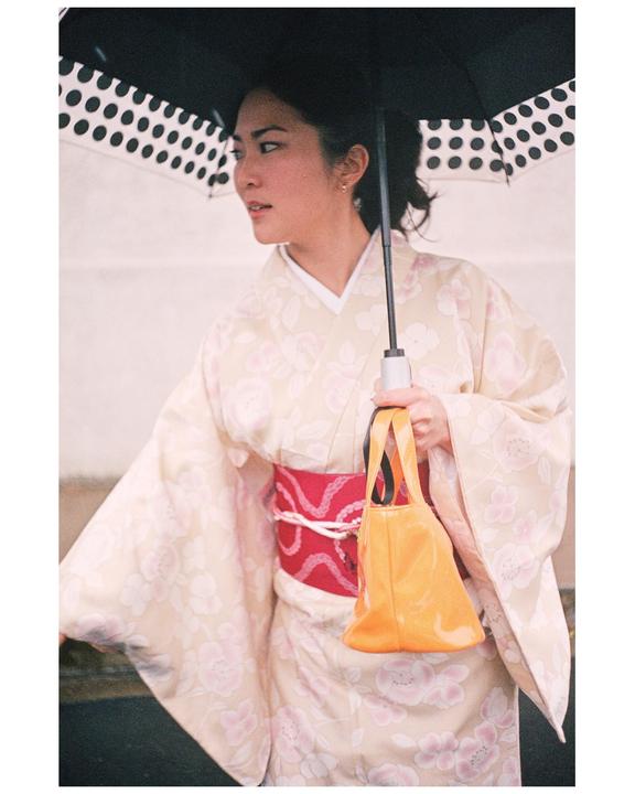 A woman in a kimono holds a polka dot umbrella and an orange handbag.