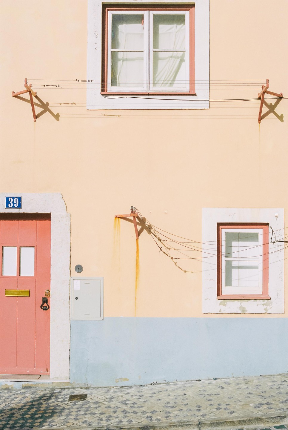 A peach-colored building with a red door and windows has clotheslines strung between two brackets on its facade.