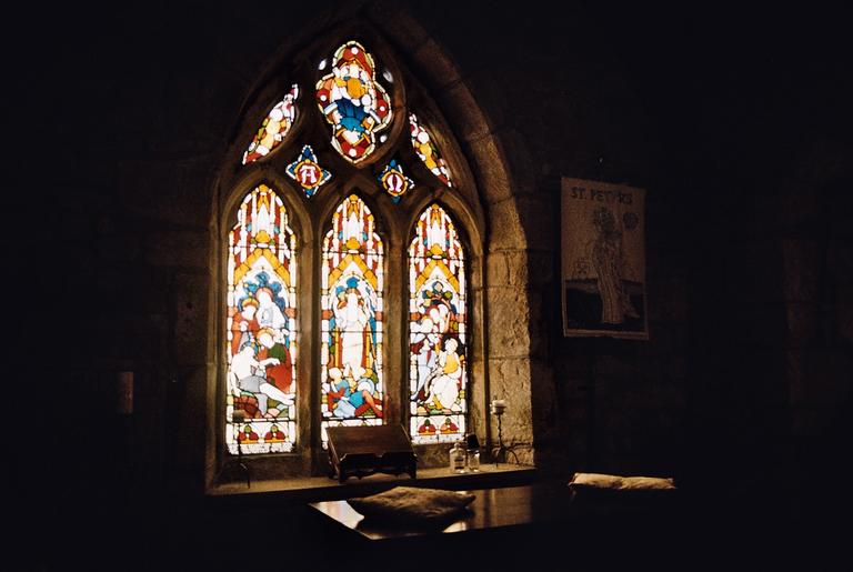 A stained glass window with religious figures is visible in a dark room.