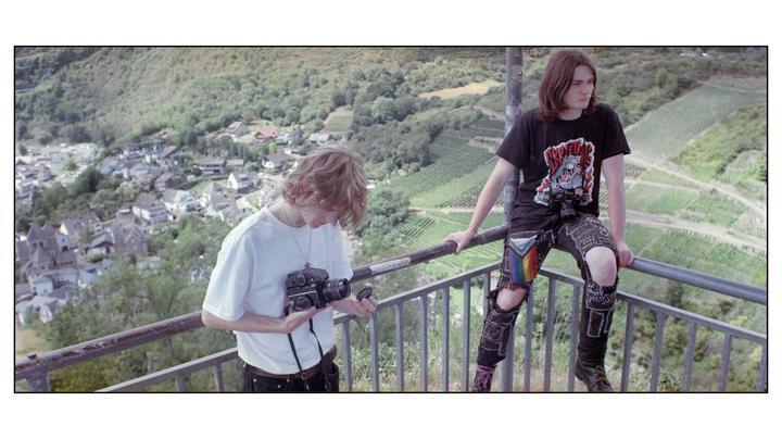 Two men are on a balcony overlooking a village and vineyards.