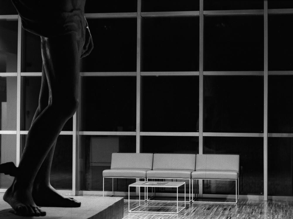 A statue of a man stands in a waiting room with a row of chairs and a table.