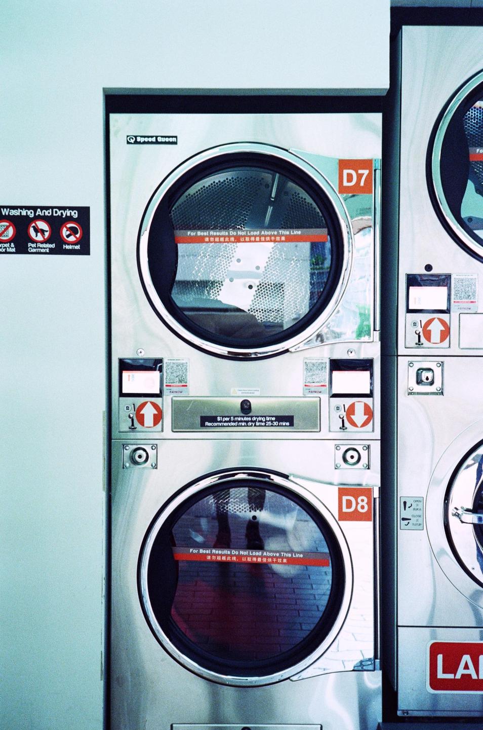 Two stacked washing machines are visible in a laundromat with a sign on the wall.
