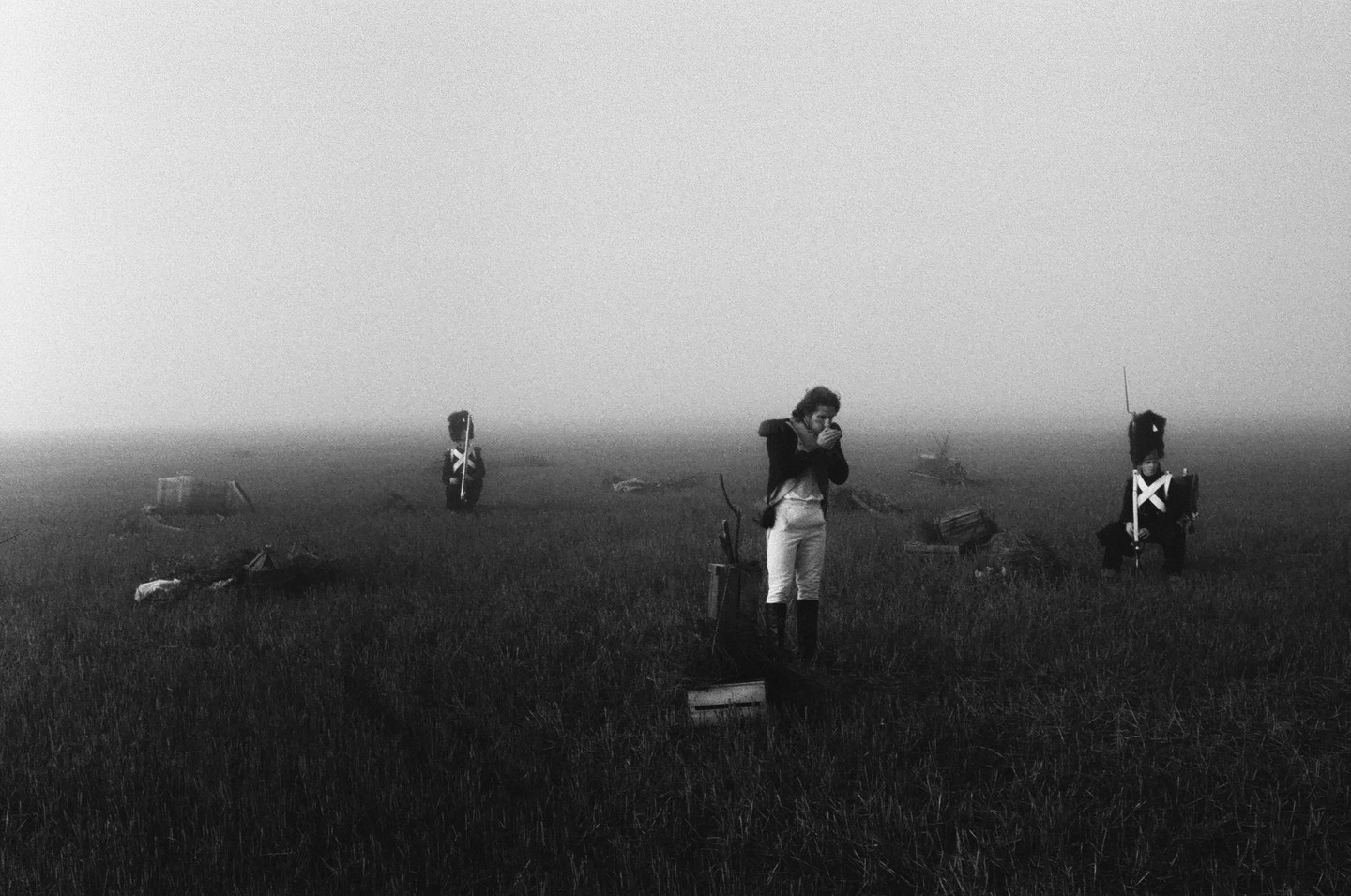 A man in period clothing lights something in a foggy field with two toy soldiers standing in the distance.