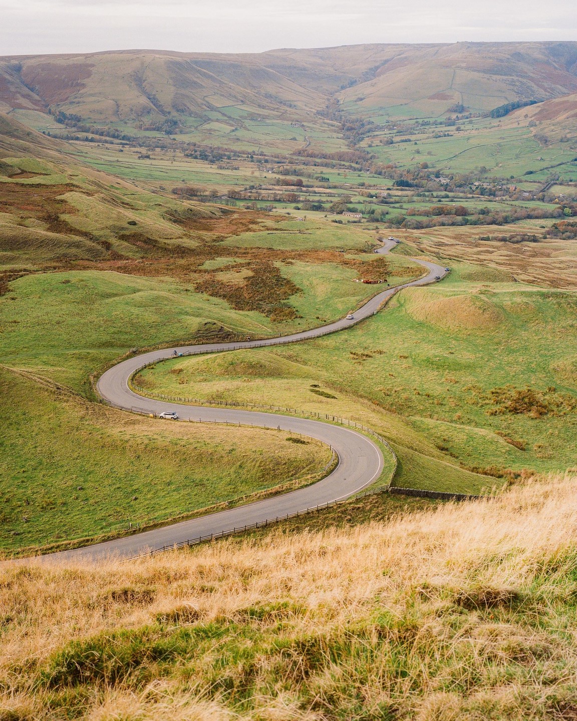A winding road curves through a green valley with hills in the background.