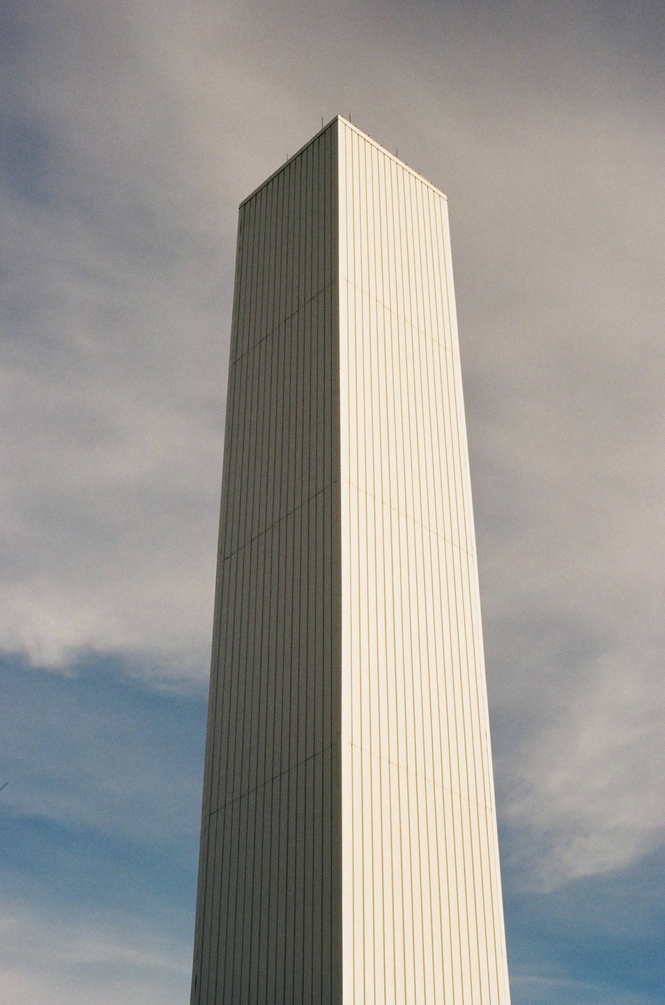 A tall, white, rectangular building stands against a cloudy sky.