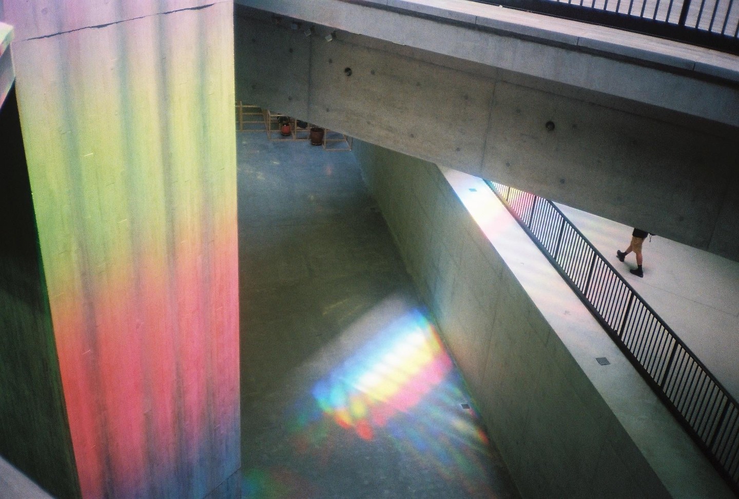 A person walks down a ramp with a black railing, while colorful light reflects on the walls and floor.