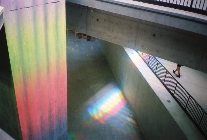 A person walks down a ramp with a black railing, while colorful light reflects on the walls and floor.