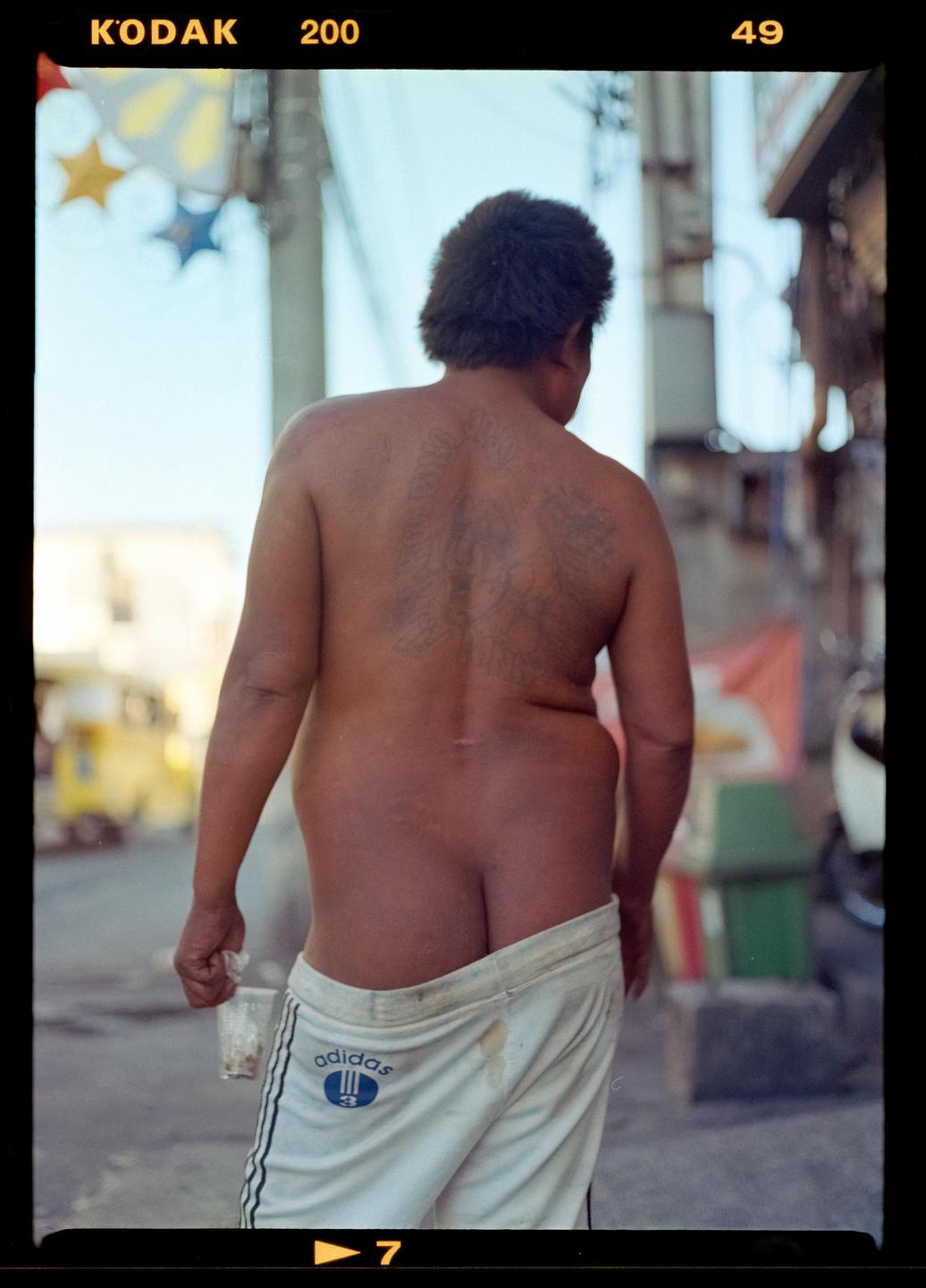 A man with tattoos on his back walks away from the camera, with his pants pulled down.