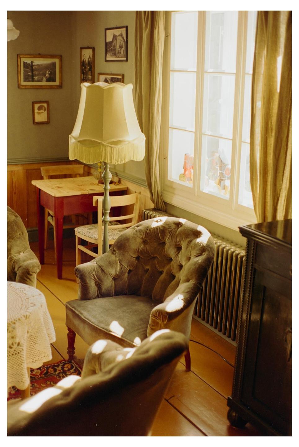 Sunlight streams through a window into a cozy room with vintage furniture and framed pictures on the wall.