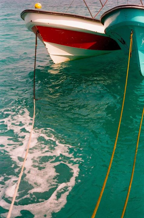 Two boats are moored in turquoise water, with ropes extending into the water.