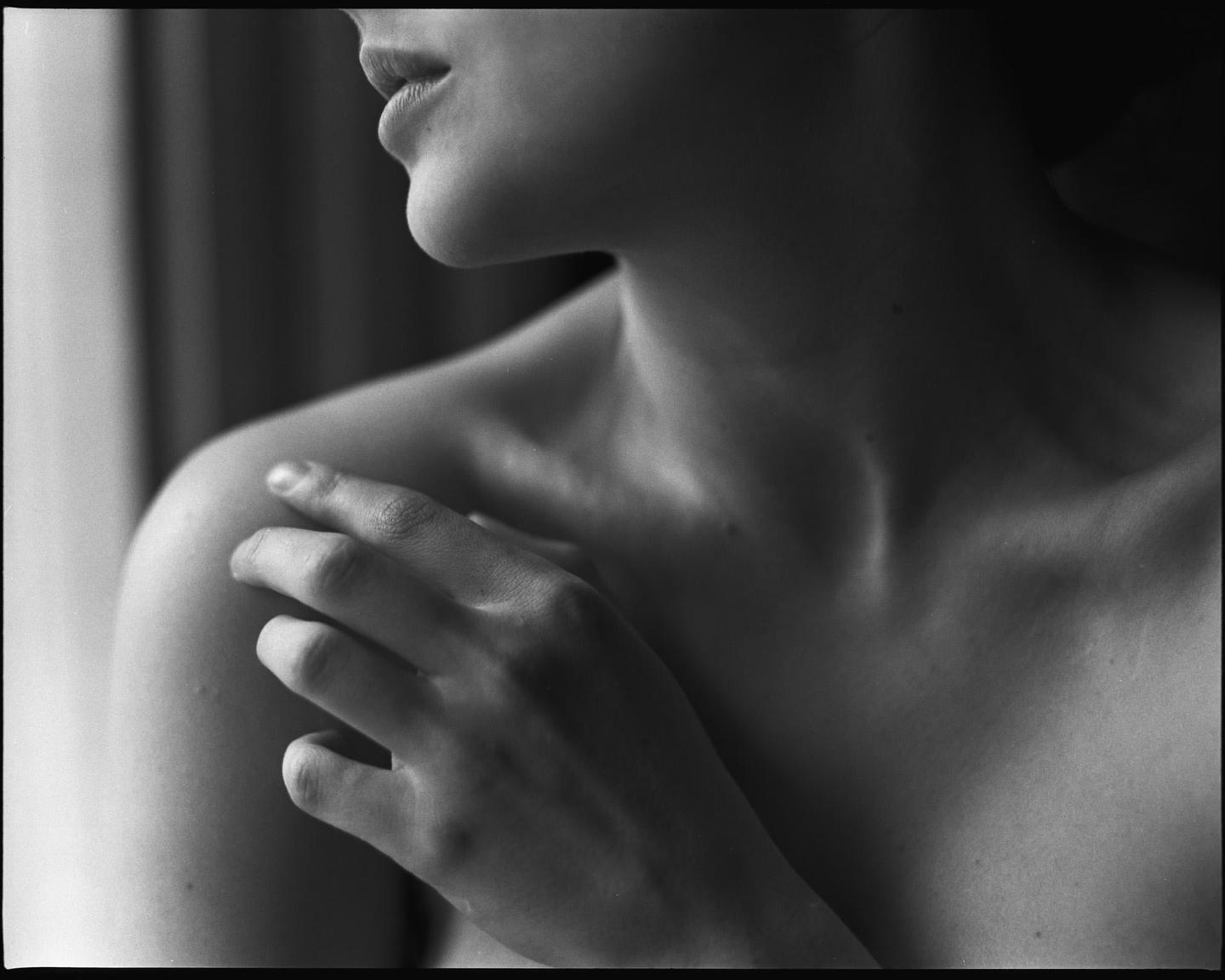 A woman's hand rests on her shoulder, with her chin and mouth visible in profile.