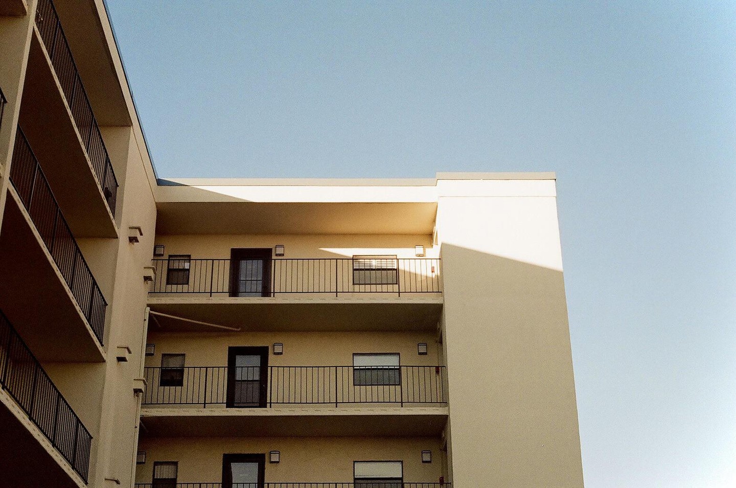 A cream-colored building with balconies is shown against a clear blue sky.