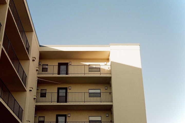 A cream-colored building with balconies is shown against a clear blue sky.
