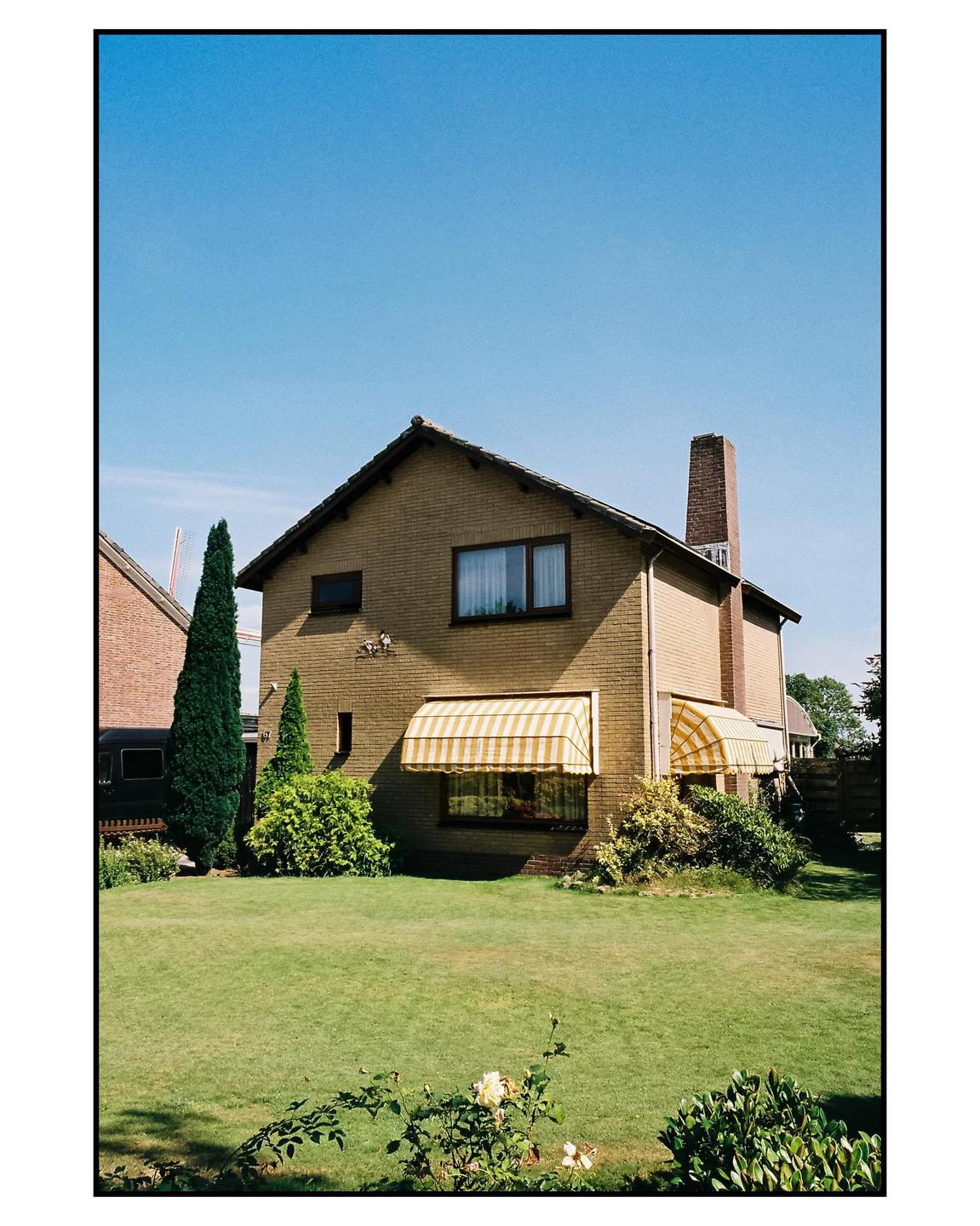 A brick house with striped awnings stands behind a green lawn under a clear blue sky.