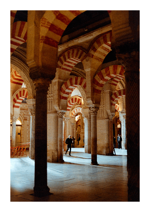 A man walks through a hall with many striped arches and columns.