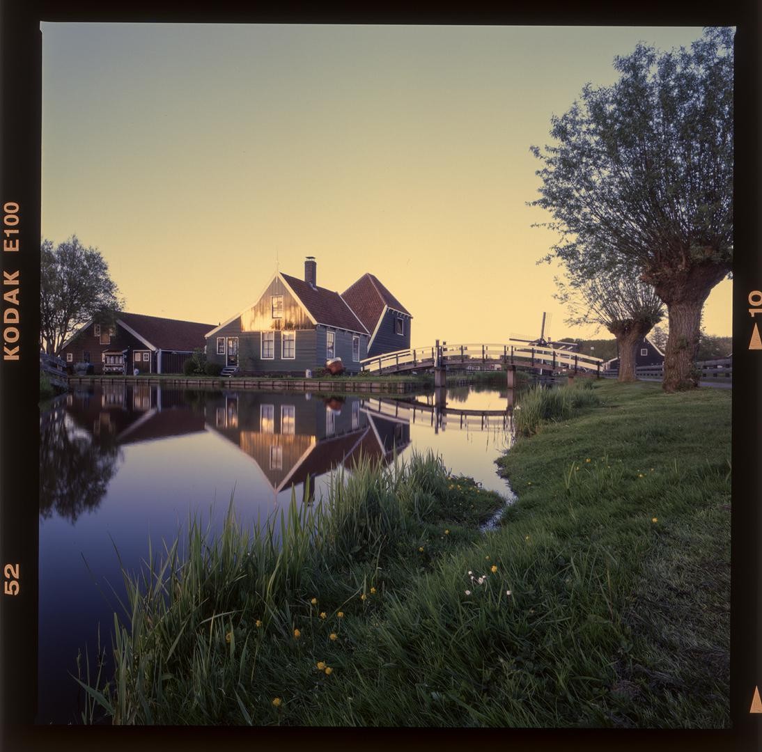 A picturesque village with houses and a bridge reflected in the water at golden hour.